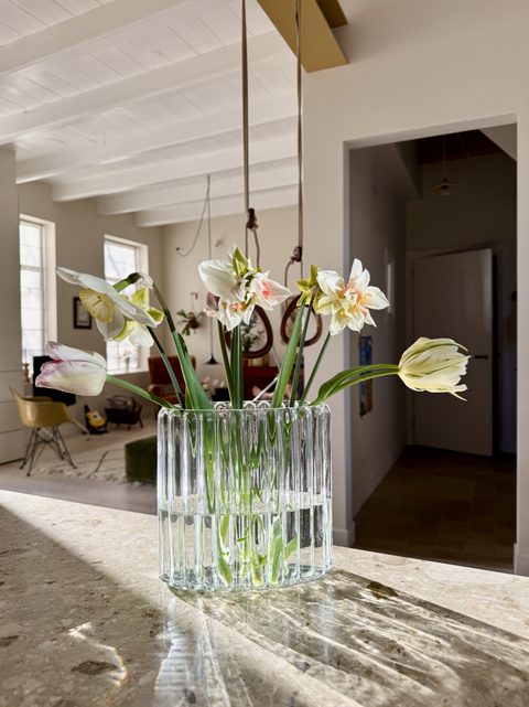 Vaas met tulpen en narcissen op het marmerresine aanrecht, met de woonkamer op de achtergrond