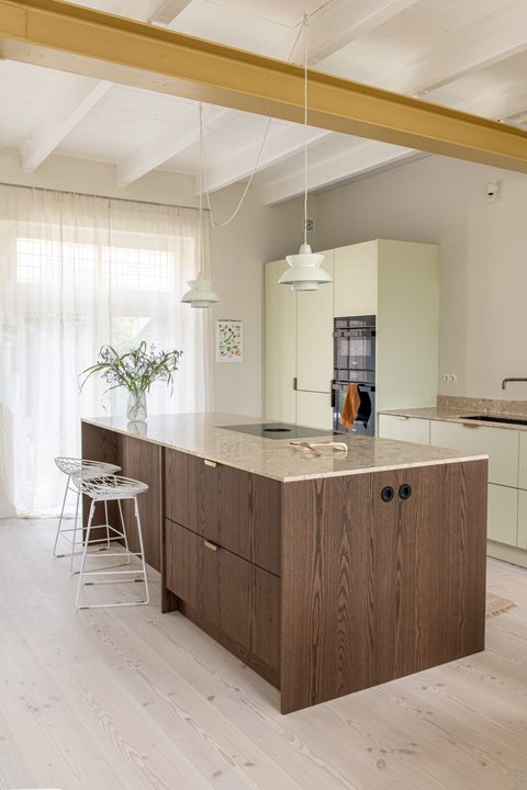 Keuken met houten kookeiland, okergele balk en lichtgroene kasten
