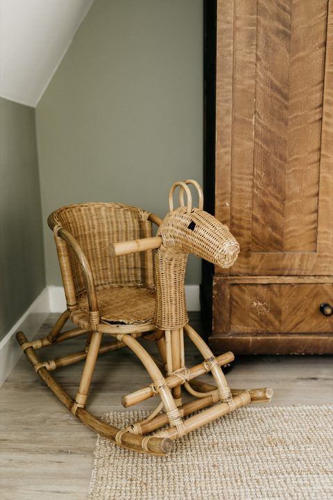 Rotan schommelpaard voor een oude houten kast in een zachtgroene kamer