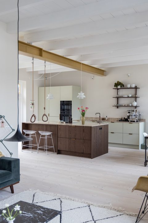 Open keuken met een donker eiken kookeiland, lichtgroene kasten, witte balken en een okergele stalen balk