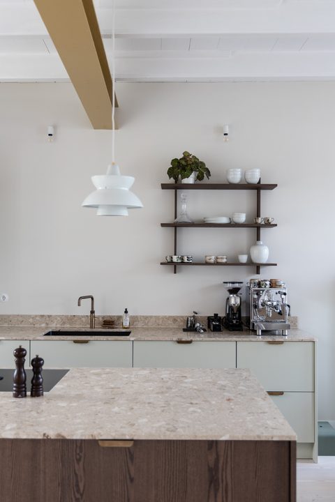 Lichtgroene keuken met terrazzo werkblad, een okergele balk en een houten wandplank met servies